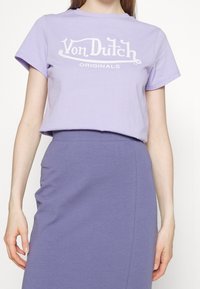 Fialové bavlněné tričko s bílým logem Von Dutch Originals, krátké rukávy a volný střih, v kombinaci s odpovídající fialovou sukní.