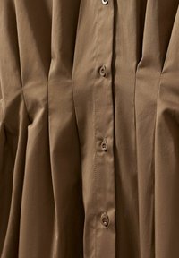 Gros plan d'un tissu marron avec des plis verticaux et une rangée de boutons assortis au centre.