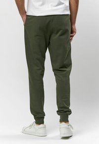Olivovo zelené jogger nohavice vyrobené z mäkkej tkaniny, s priliehavými manžetami, bočnými vreckami a voľným strihom, skombinované s bielymi teniskami.