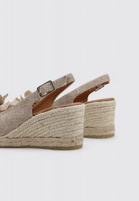 Sandales compensées beiges avec un dessus en tissu texturé, une sangle de cheville réglable et un talon en jute entouré d'une semelle lisse marron.