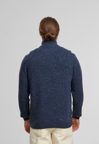 Marineblau gestrickter Pullover mit hohem Kragen, strukturiertem Oberflächenmaterial und gesprenkeltem Muster. Verfügt über lange Ärmel sowie gerippte Bündchen und Saum.