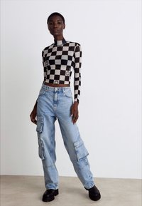 Black and white checkered long-sleeve crop top paired with light blue cargo jeans, featuring pockets and black platform boots.