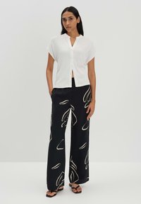 Blusa bianca a maniche corte con texture e chiusura a bottoni, abbinata a pantaloni neri a vita alta con un motivo astratto color crema.