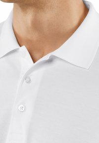Polo shirt bianco con colletto classico, tessuto texture e due bottoni trasparenti. La vista ravvicinata mette in risalto i dettagli della cucitura e del tessuto.