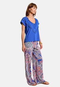 Top de algodón azul con borde de encaje, combinado con pantalones amplios de patrón claro que presentan un diseño paisley en rosa y azul. Se llevan sandalias simples.
