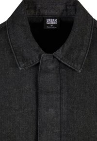 Giacca in denim nera con collo, chiusura a bottoni e finitura strutturata. Etichetta con la scritta "URBAN CLASSICS", taglia M, prodotta in Pakistan.