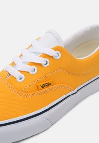 Baskets en toile jaune avec lacets blancs, œillets ronds et semelle en caoutchouc. Comprend une étiquette avec le logo Vans sur le côté et des coutures contrastantes.