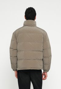 Geacă matlasată maro deschis cu guler înalt, textură în formă de romburi, manșete elastice și croială largă. Purtați cu blugi închiși la culoare.