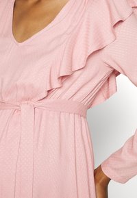 Vestido rosa claro com mangas franzidas, decote em V, cintura ajustada com um laço e tecido texturizado com um padrão subtil.