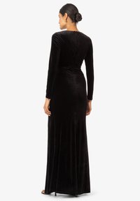 Schwarzes Samt-Kleid mit langen Ärmeln, das ein figurbetontes Oberteil und einen fließenden Rock aufweist, mit einem dezenten Reißverschlussdetails hinten. Glatte Textur im gesamten Kleid.
