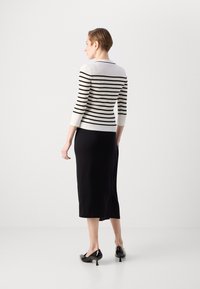 Pull en tricot rayé blanc et noir, à manches trois-quarts, associé à une jupe midi noire et des escarpins noirs à bout pointu.