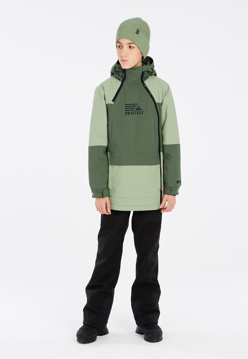 Giacca da sci verde con accenti neri, dotata di cappuccio, logo sul petto e tasca anteriore, abbinata a pantaloni da neve neri e stivali.