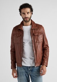 Brun läderjacka med dragkedja fram, två bröstfickor och krage. Har en något strukturerad yta och en figursydd design.