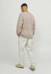 Maglione a maglia color beige chiaro con spalle cadute, abbinato a pantaloni cargo bianchi. L'outfit presenta una vestibilità comoda e una texture morbida.