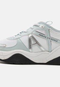 Sneaker bianca con accenti azzurri chiari, dotata di un logo "A" argento, pannelli testurizzati e suola in gomma nera. Progettata con chiusura con lacci.