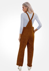 Tirantes de sarga marrón con piernas anchas y ajustables, con una textura suave y un detalle de bolsillo trasero.