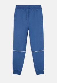 Pantalones de chándal azules hechos de una tela suave, con un diseño ajustado y piping en contraste en la zona de las rodillas y una cinturilla elástica.