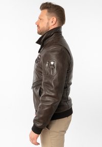 Bruine leren bomberjack met een hoge kraag, ribbelmanchetten, twee zijzakken en een mouwzak met een rits en patchdetail.