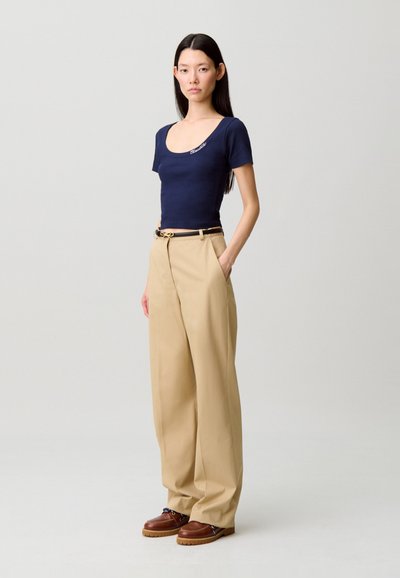Top de manga corta azul marino con escote en forma de media luna, combinado con pantalones beige de pierna ancha y talle alto, y calzado marrón con suela texturizada.