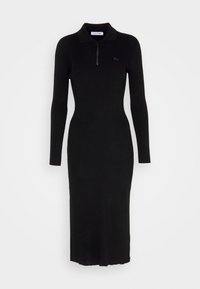 Robe noire en tricot avec des manches longues et un col zippé, présentant une texture côtelée et une silhouette ajustée, descendant en dessous du genou.