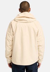 Beige huppari, jossa on rento malli, elastiset hihansuut ja pyöristetty helma. Ominaisuuksiin kuuluu minimalistiinen muotoilu ja sileä pinta.