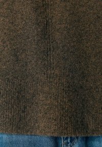 Brauner strukturierter Pullover mit einem weichen, flauschigen Aussehen und geradem Saum. Kombiniert mit blauen Jeans für einen lässigen Look.