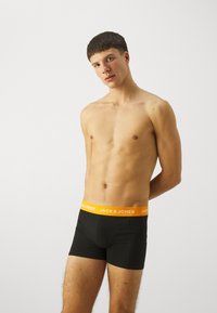 Zwarte boxershort met een oranje tailleband waarop "JACK & JONES" in witte tekst staat, gemaakt van een zachte, rekbare stof.