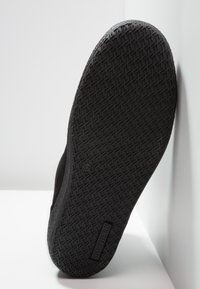 Semelle de chaussure noire avec un motif de grip texturé. Présente une forme plate et un marquage sur le côté, conçue pour la durabilité et l'adhérence.
