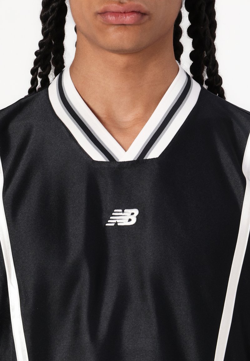 T-shirt sportif noir avec un col en V, comportant des rayures blanches le long du col et des côtés. Inclut un petit logo blanc au niveau de la poitrine.