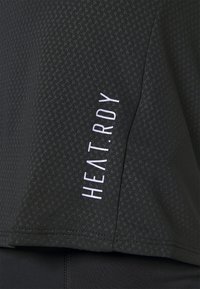 Svart sporttopp med ett texturerat mönster och vit "HEAT.RDY"-logotyp tryckt vertikalt på sidan. Mjuk och lättviktslängd.