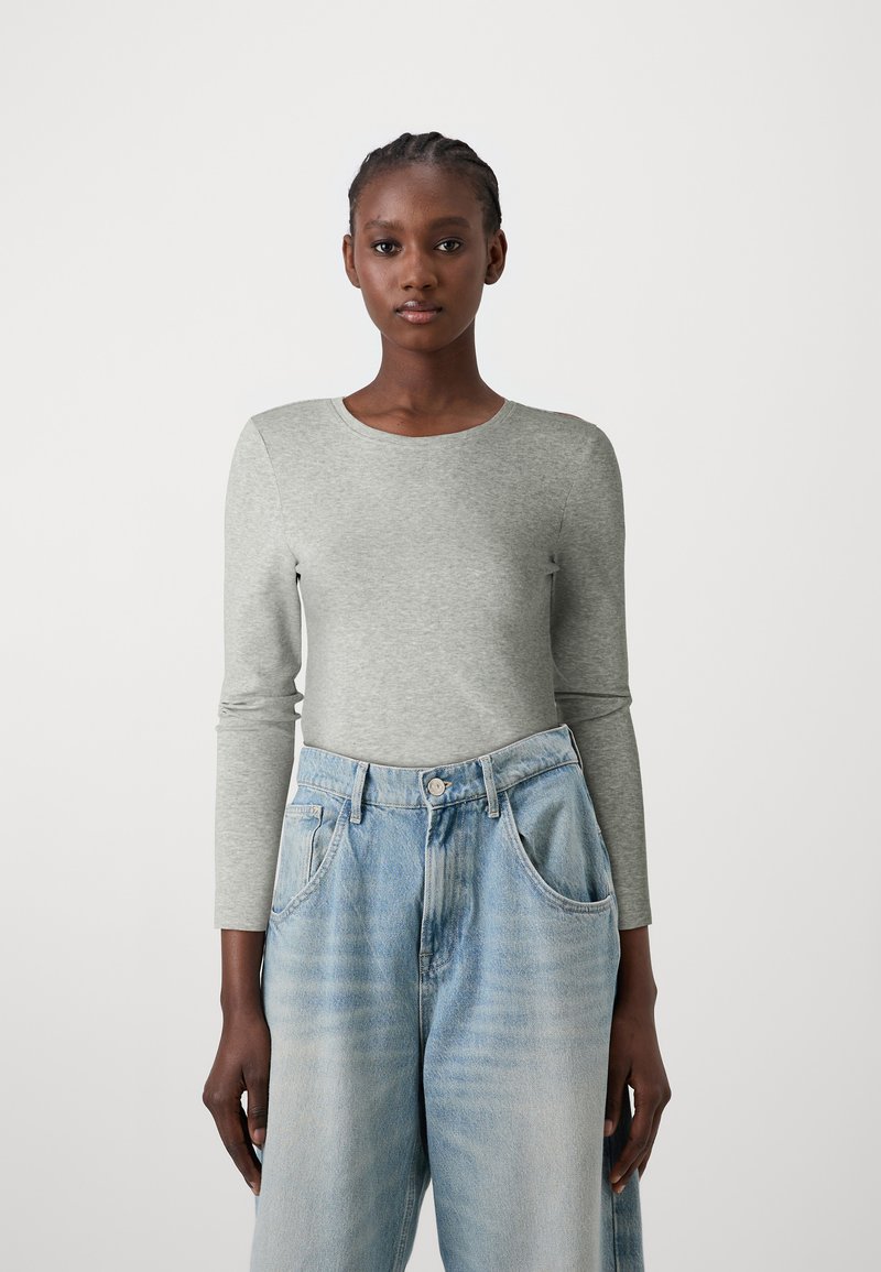 Chemise grise à manches longues en mélange de coton, associée à un jean taille haute bleu clair. La chemise présente un col rond et une silhouette ajustée.
