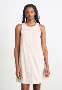 Vestido sin mangas de color beige claro, con escote redondo, tejido texturizado, de longitud media, que presenta costuras mínimas y bolsillos laterales.