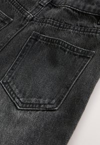 Gros plan sur un tissu en denim noir montrant une poche arrière cousue et les détails des coutures d'un jean.