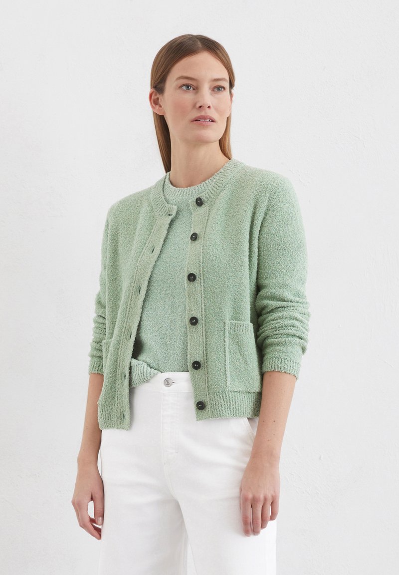 Mint green cardigan with a textured knit, featuring a round neckline, black buttons, and front pockets, paired with a matching top and white pants.