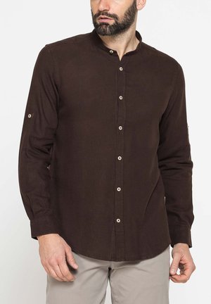 Uomo che indossa una camicia marrone scuro a maniche lunghe con bottoni e collo alla coreana e pantaloni grigio chiaro su sfondo bianco uni.