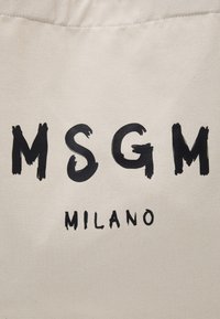 Lettres noires style coups de pinceau formant MSGM au-dessus d'un texte plus petit indiquant MILANO sur un fond en tissu beige.