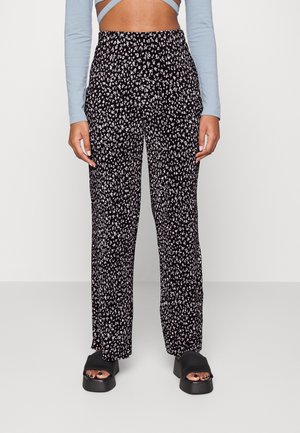 Schwarze Hosen mit einem weißen Blumenmuster, lockere Passform, elastischer Bund und Vordertaschen, kombiniert mit schwarzen Sandalen mit offenen Zehen.