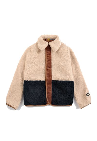 Veste polaire avec partie supérieure et manches beiges, partie inférieure noire, bordure et col marron, manches longues, et petite étiquette rectangulaire sur le poignet gauche.