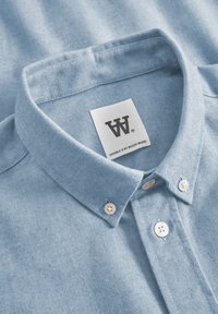 Light blue button-up shirt with a textured fabric, featuring a classic collar, white buttons, and a label that reads "DOUBLE V BY WOOD WOOD."