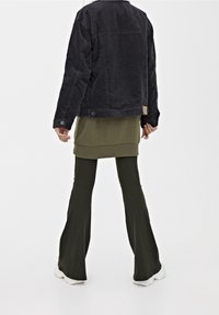 Svart kordjacka, olivgrön lagerblus och flareade olivfärgade byxor. Jackan har en etikett, och vita sneakers fulländar outfiten.