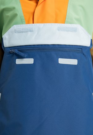 Bunte wasserdichte Jacke mit grünen, orangen und blauen Paneelen. Sie verfügt über eine Reißverschlusstasche mit Klappe und strukturierten Klettverschluss-Akzenten.