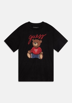 Black cotton t-shirt featuring a cartoon bear in a red sweater with a triangular logo, sitting with denim pants, and "guess" text above.