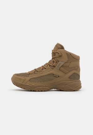 Brązowy taktyczny botek typu high-top z panelami z siateczki, wyściełanym kołnierzem, grubą podeszewką z bieżnikiem i sznurowadłami, przedstawiony z profilu na białym tle.