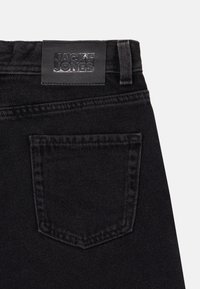 Il taschino posteriore e la vita di un paio di jeans in denim nero con etichetta cucita che recita "JACK & JONES" su uno sfondo semplice.