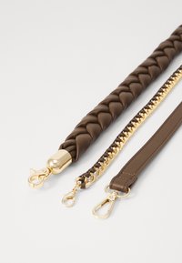 Tre cinturini: uno in pelle intrecciata marrone con accessori in oro, uno in pelle marrone con catene e un cinturino in pelle marrone semplice con ganci.