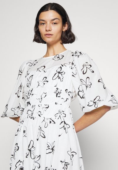 Άσπρο φόρεμα με μαύρα λουλούδια, φουσκωτά μανίκια και εφαρμοστό μέσο, φτιαγμένο από ελαφρύ ύφασμα με απαλή αφή.