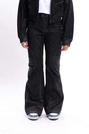 Pantaloni neri a campana realizzati in tessuto testurizzato, con dettagli delle cuciture curve e tasche frontali, abbinati a sneaker blu e bianche.