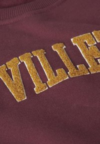 Burgundské crewneck mikiny s texturovaným žlutým vyšíváním, které hlásá "VILLET." Disponuje žebrovaným výstřihem a měkkou texturou látky.