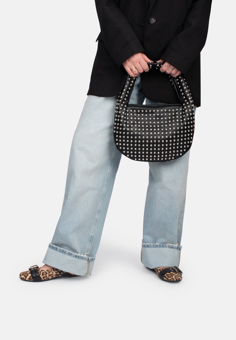 Bolso de cuero negro con tachuelas plateadas, asa curvada, combinado con jeans de pierna ancha de color azul claro y sandalias deslizantes con estampado animal.