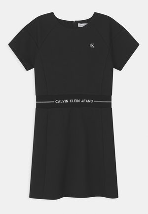 Czarna sukienka z krótkimi rękawami, okrągłym dekoltem i dopasowanym talią. Posiada pasek z logo Calvin Klein Jeans w talii. Gładka tekstura materiału.